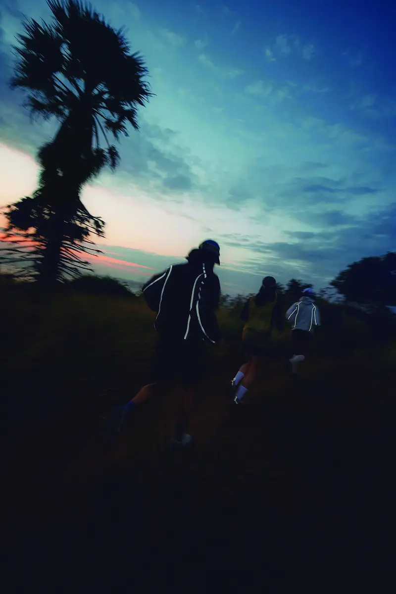 AEON® runners on a hillside trail at dusk beneath a palm tree