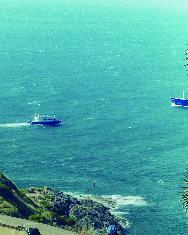 Boats crossing a turquoise bay below a rocky headland
